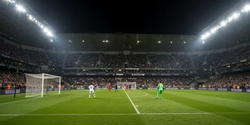 Football player taking a penalty kick in a packed stadium at night.